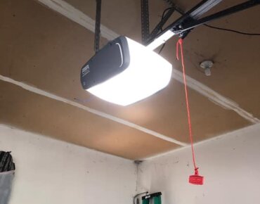 Close-up of a garage door opener with a red garage door emergency release cord hanging down.