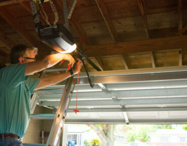 Technician performing a garage door emergency release to fix a malfunctioning garage door opener system.