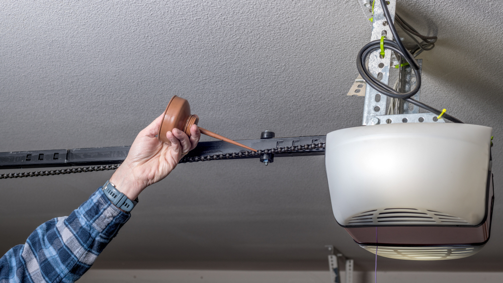 Homeowner performing garage door tune-up by lubricating chain mechanism to ensure smooth and reliable operation.