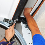 Technician performing emergency garage door repairs on overhead track system using wrench to restore safe function.