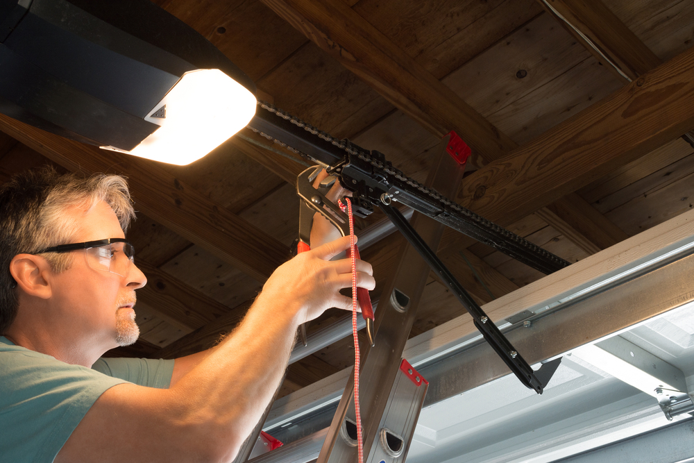 Man repairing a faulty garage door opener, handling electrical wiring while standing on a ladder.