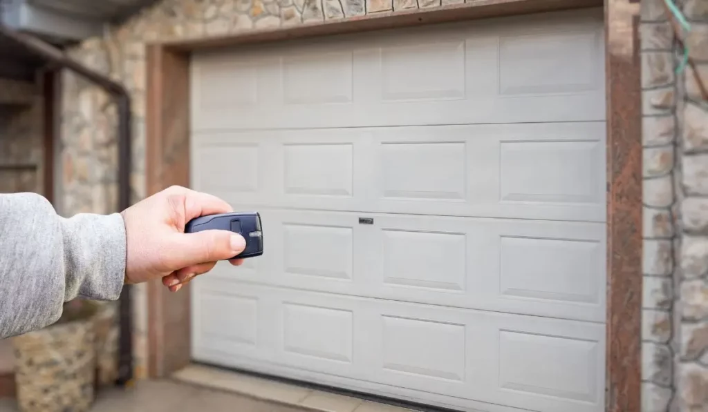 Hand using remote control to operate a garage door, highlighting commercial garage doors vs. residential differences.