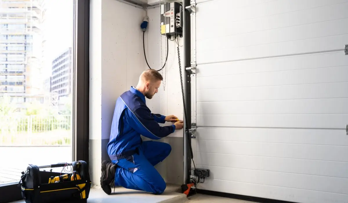 Garage door technician checking safety cables during summer maintenance tune-up.