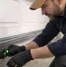 Technician adjusting garage door sensor alignment near bottom track to restore safe automatic garage door closing operation.