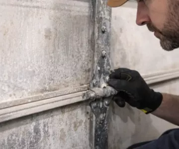 Technician inspecting garage door hinge corrosion demonstrating how to prevent rust during winter garage door maintenance.