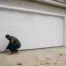 Homeowner performing fall garage door maintenance by inspecting the bottom weather seal before winter weather arrives.